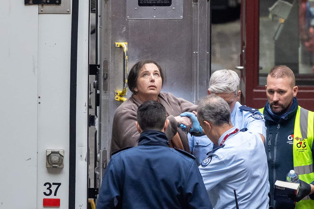 A woman is being led out of a prison van by officers.