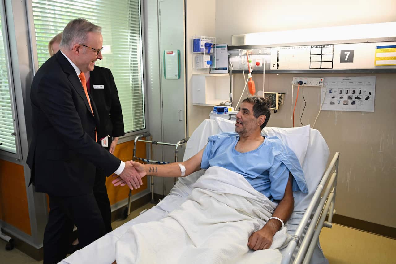 Anthony Albanese, in a suit, shakes hands with a man in a hospital bed.