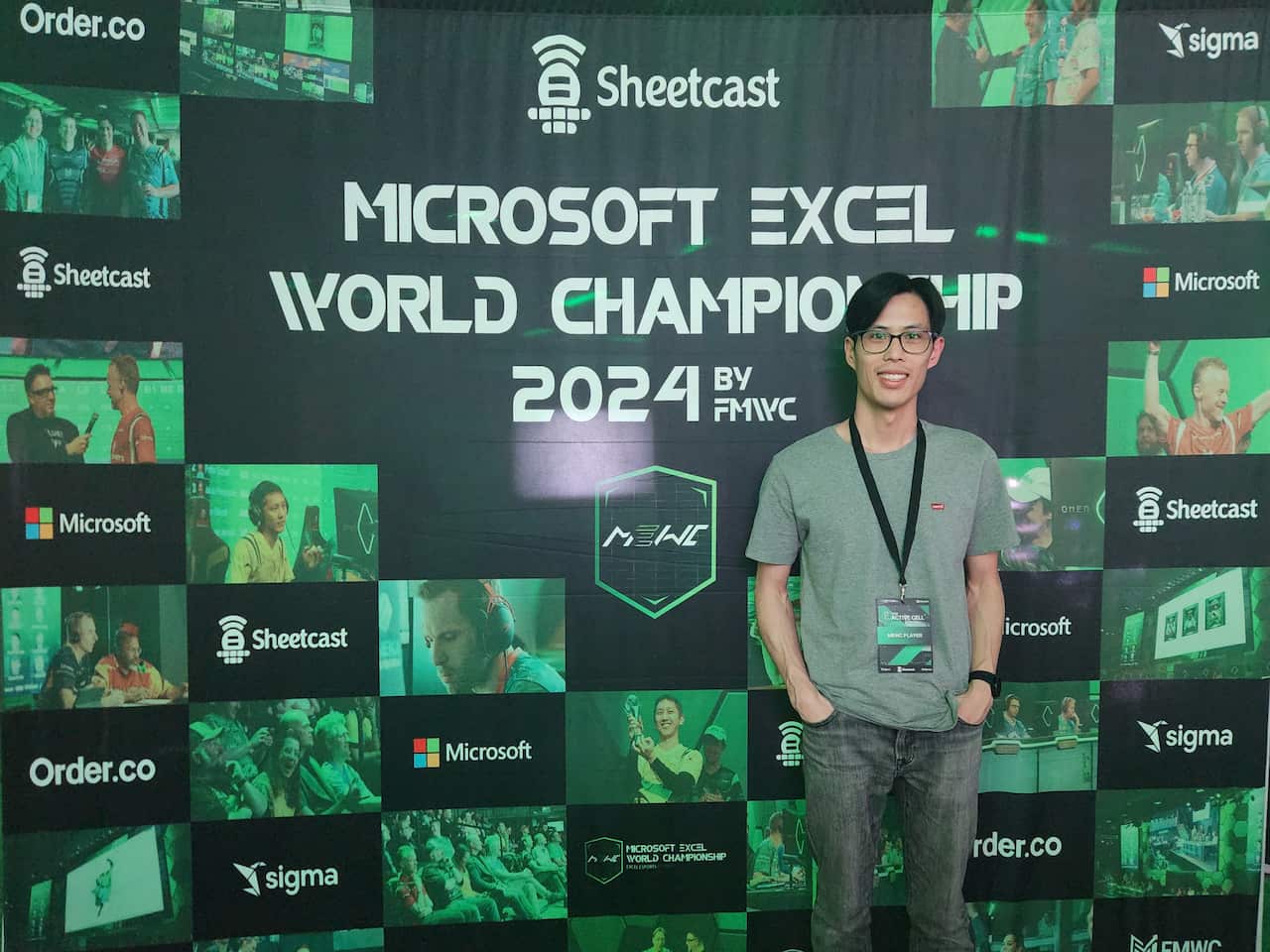 A man smiling in front of a sign that says 'Microsoft Excel World Championship 2024'