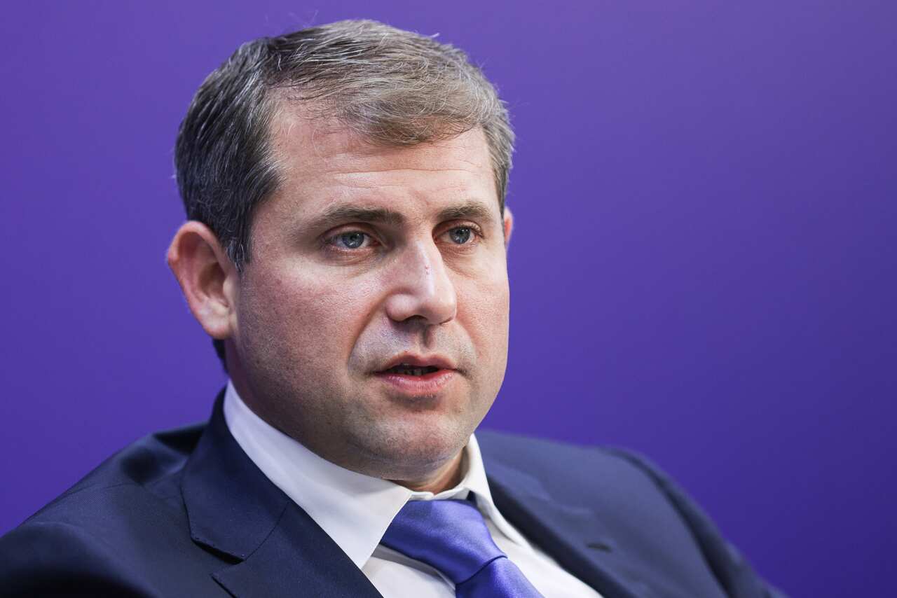 A man, wearing a suit and tie, is speaking.