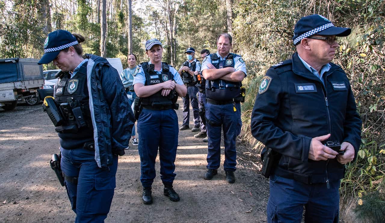 NSW police officers standing on a dirt road amongst forest area