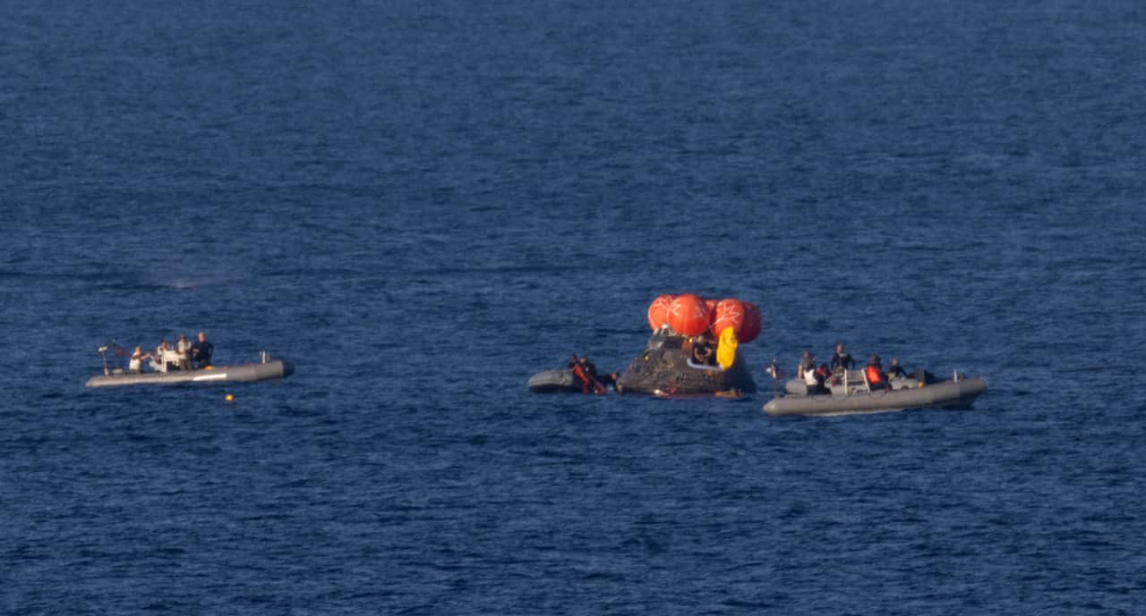 Small boats surrounding a floating space capsule floating in the ocean