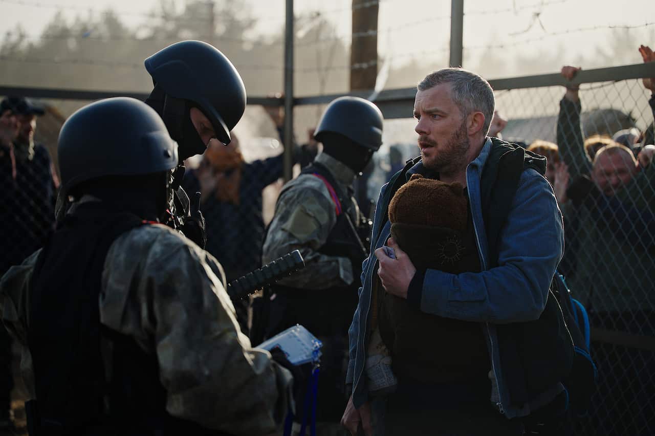 A man holds onto a child as he stands in front of riot police