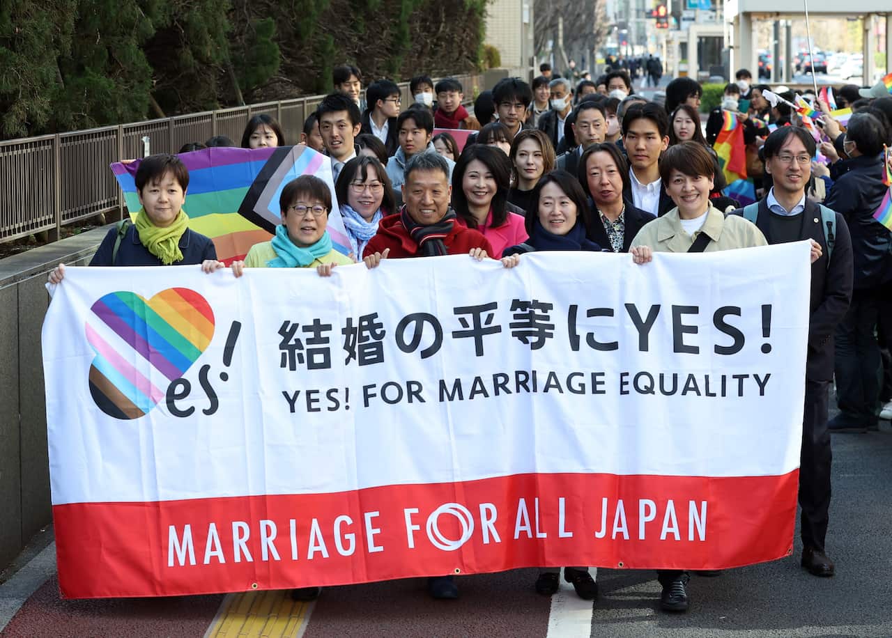 A group of people march along a road holding a large banner