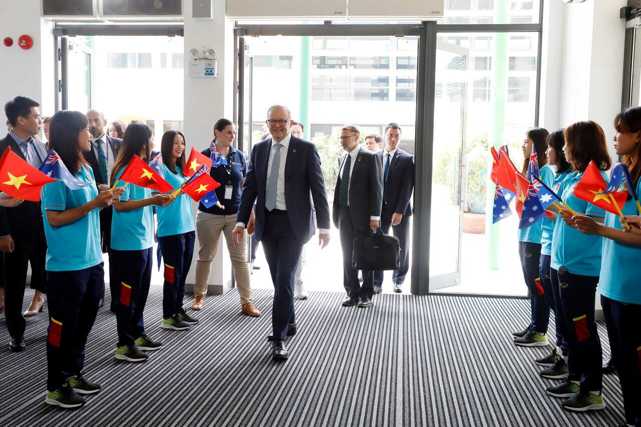 Anthony Albanese arrives at a school. Students are waving Vietnamese and Australian flags.