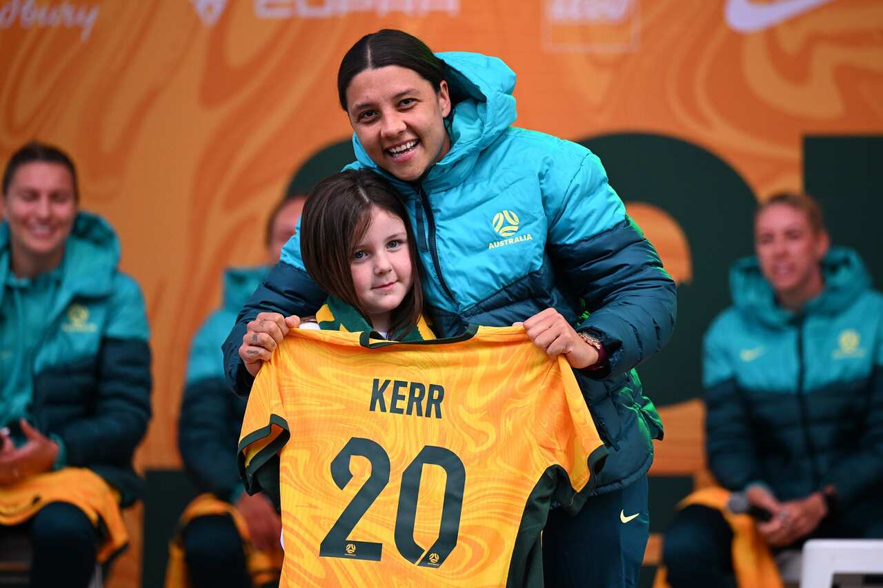 Sam Kerr (right) holds a jersey with her name and number 20 on it as she hugs a young female fan at Federation Square in Melbourne on 11 July 2023. 