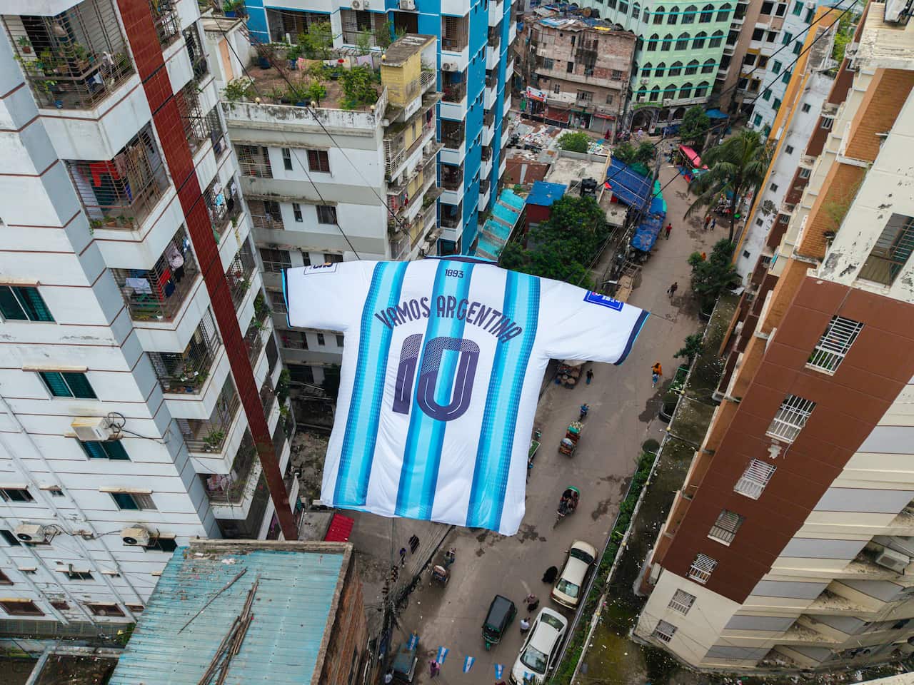 A Giant Argentina jersey hanging above a city street, alongside tall buildings.