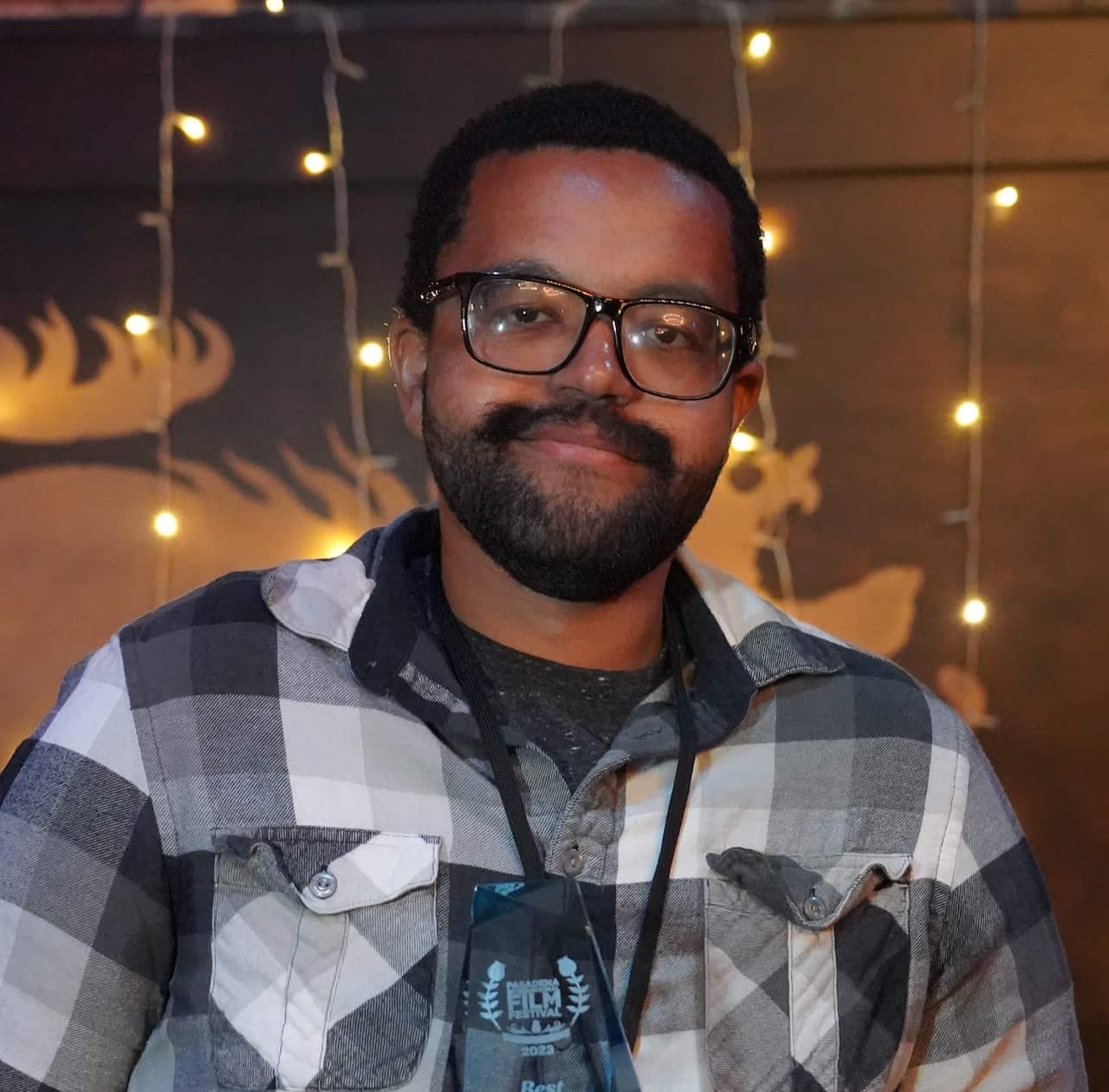 A man wearing a plaid shirt and glasses holding a card up.