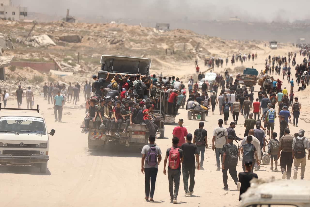 People walking along a dirt road. Trucks carrying groups of people.
