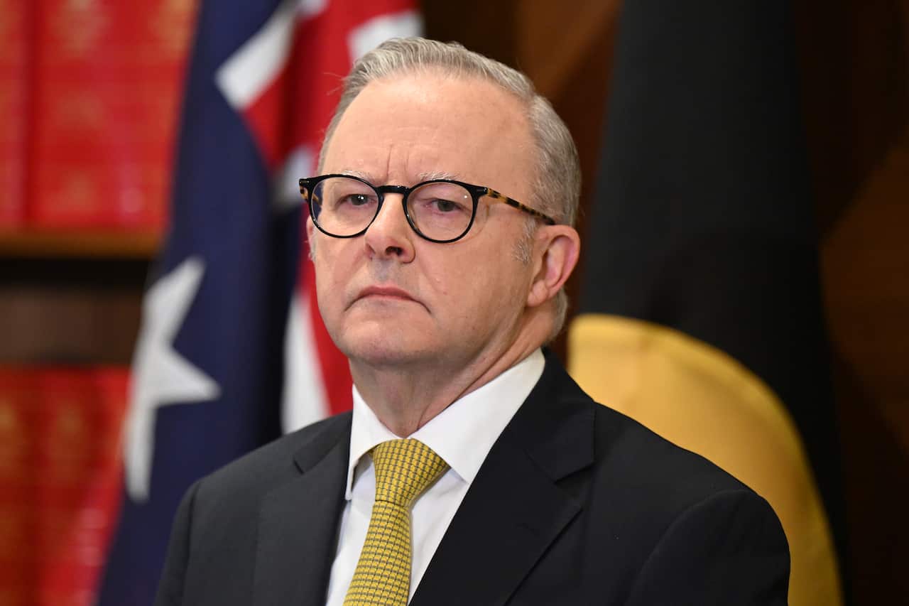 Anthony Albanese wearing a suit with a yellow tie, standing in front of Australian flat