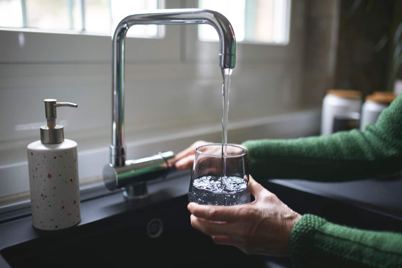 A woman pouring a glass of water from a tap. 