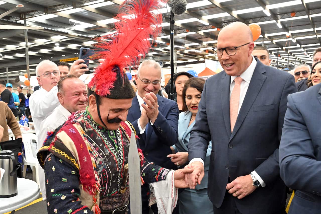A man dressed in a traditional outfit holds the hand of a smiling Peter Dutton