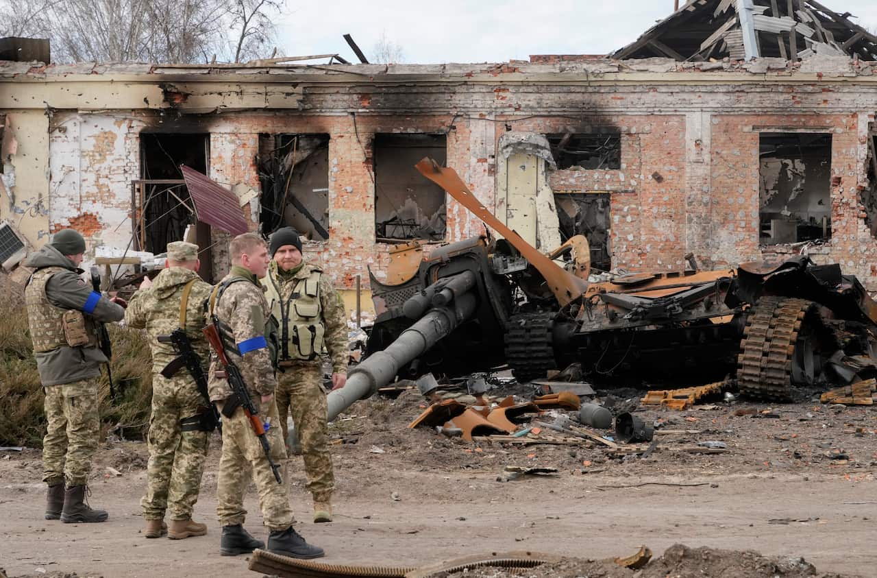 Ukrainian soldiers are seen standing next to debris from a Russian tank.