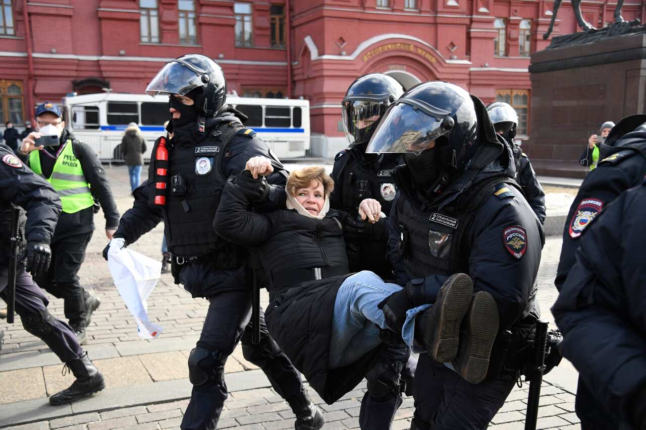 Police officers are seen detaining a woman during a protest against Russian military action in Ukraine.