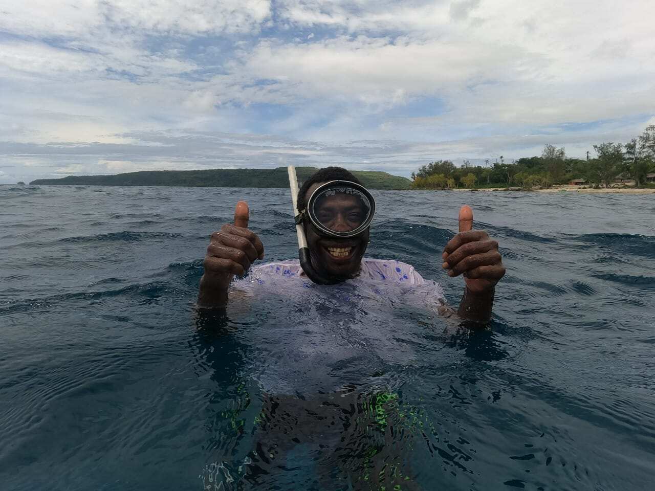 A man in snorkelling equipment standing in the ocean.