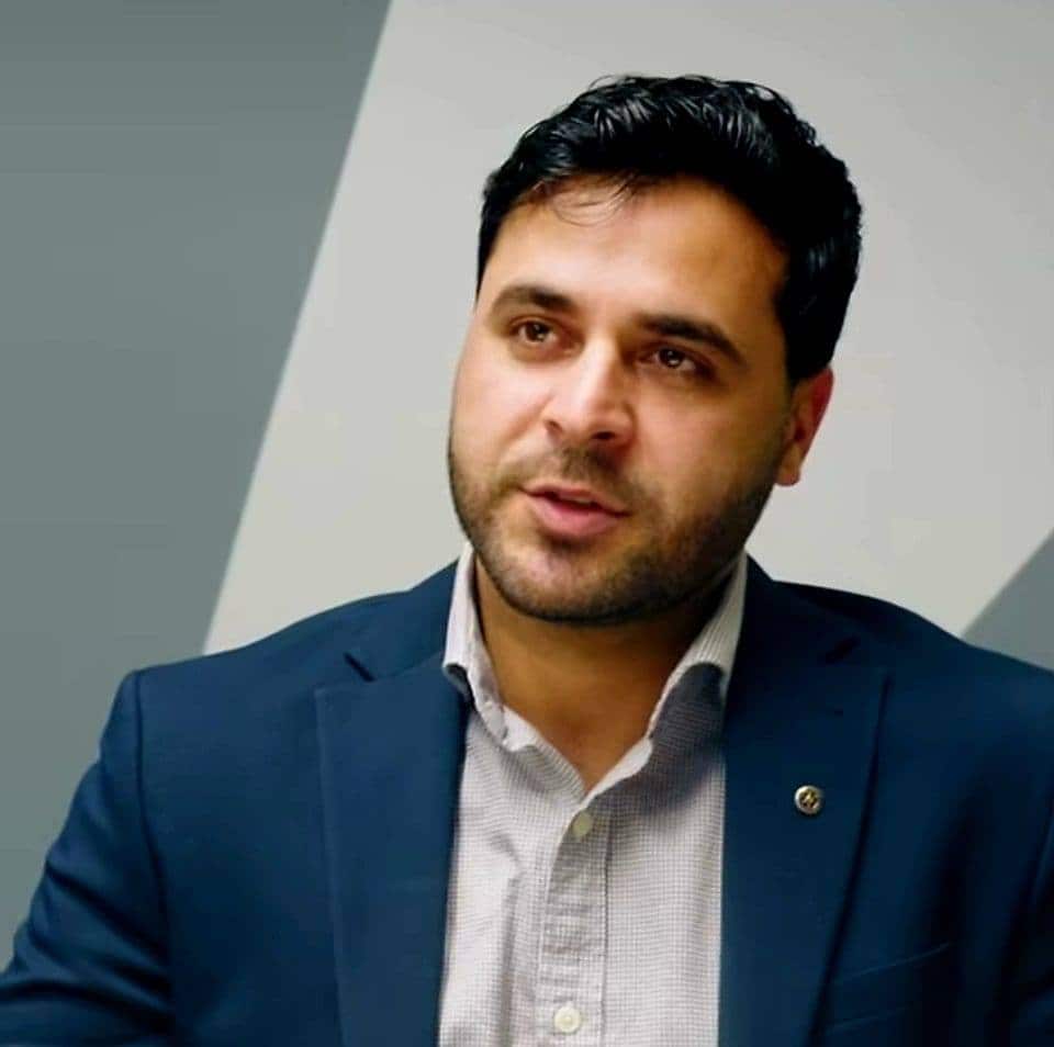 A man wearing a dark blue blazer and light blue shirt.