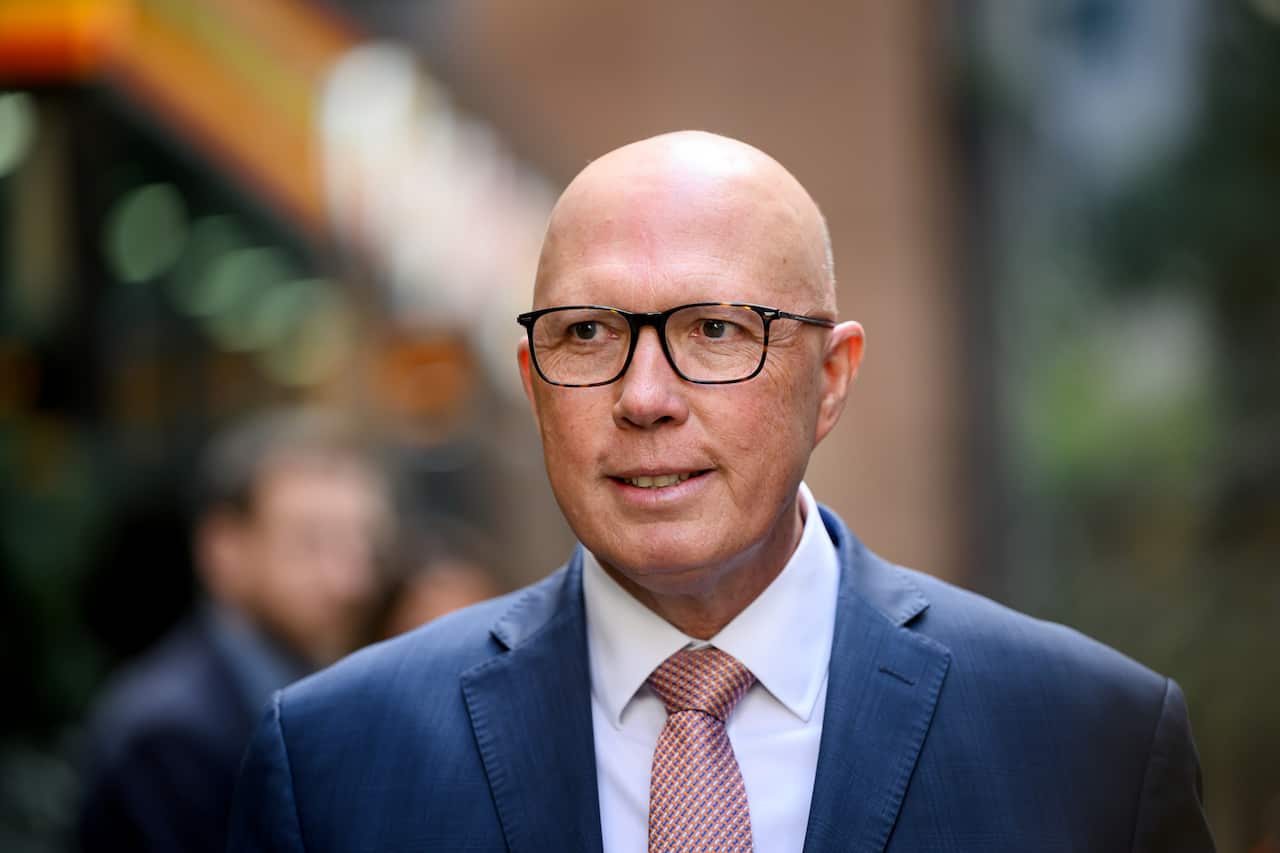 A close-up shot of Peter Dutton smiling wearing a blue suit white shirt pink tie and black gladses