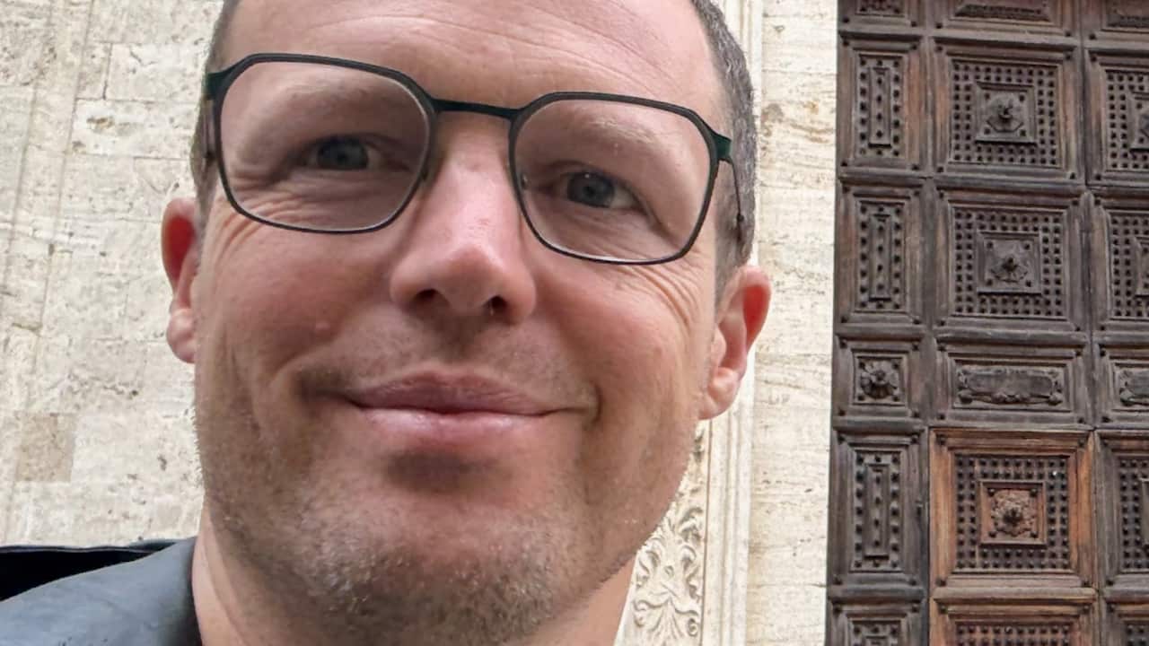 a closeup of a middle age man in glasses in front of a european church