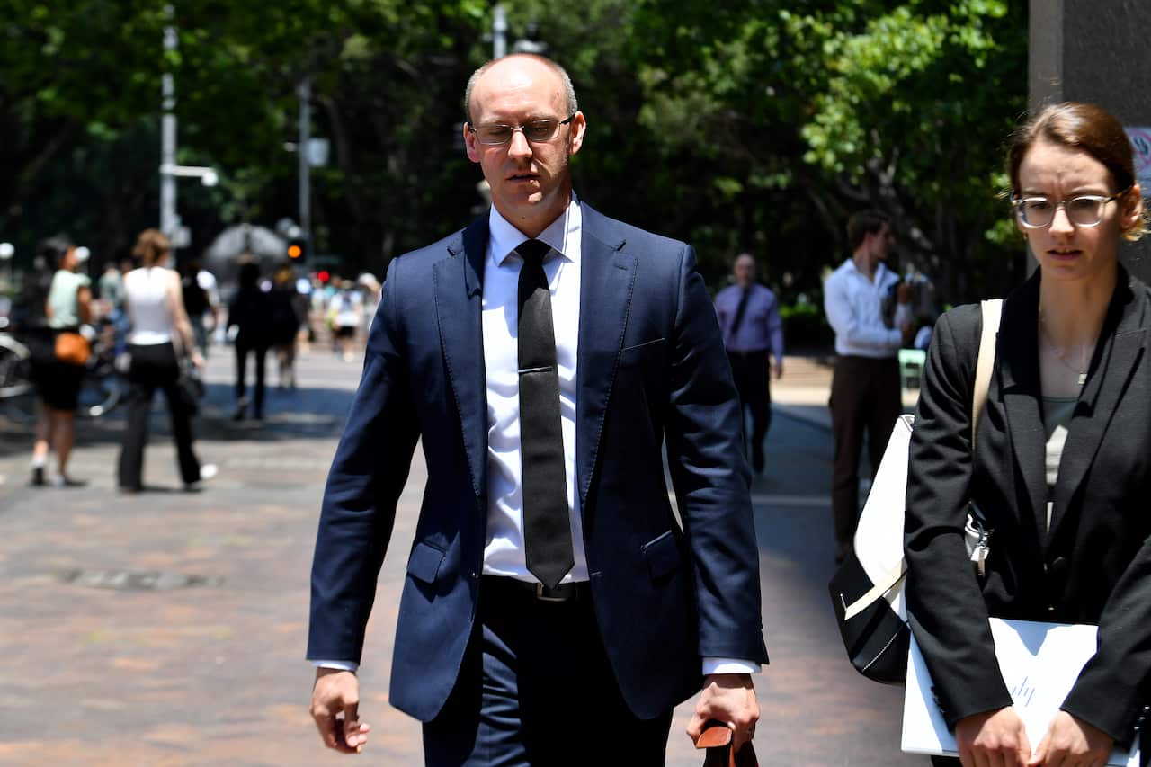 A man wearing a suit, tie and glasses walking outside.