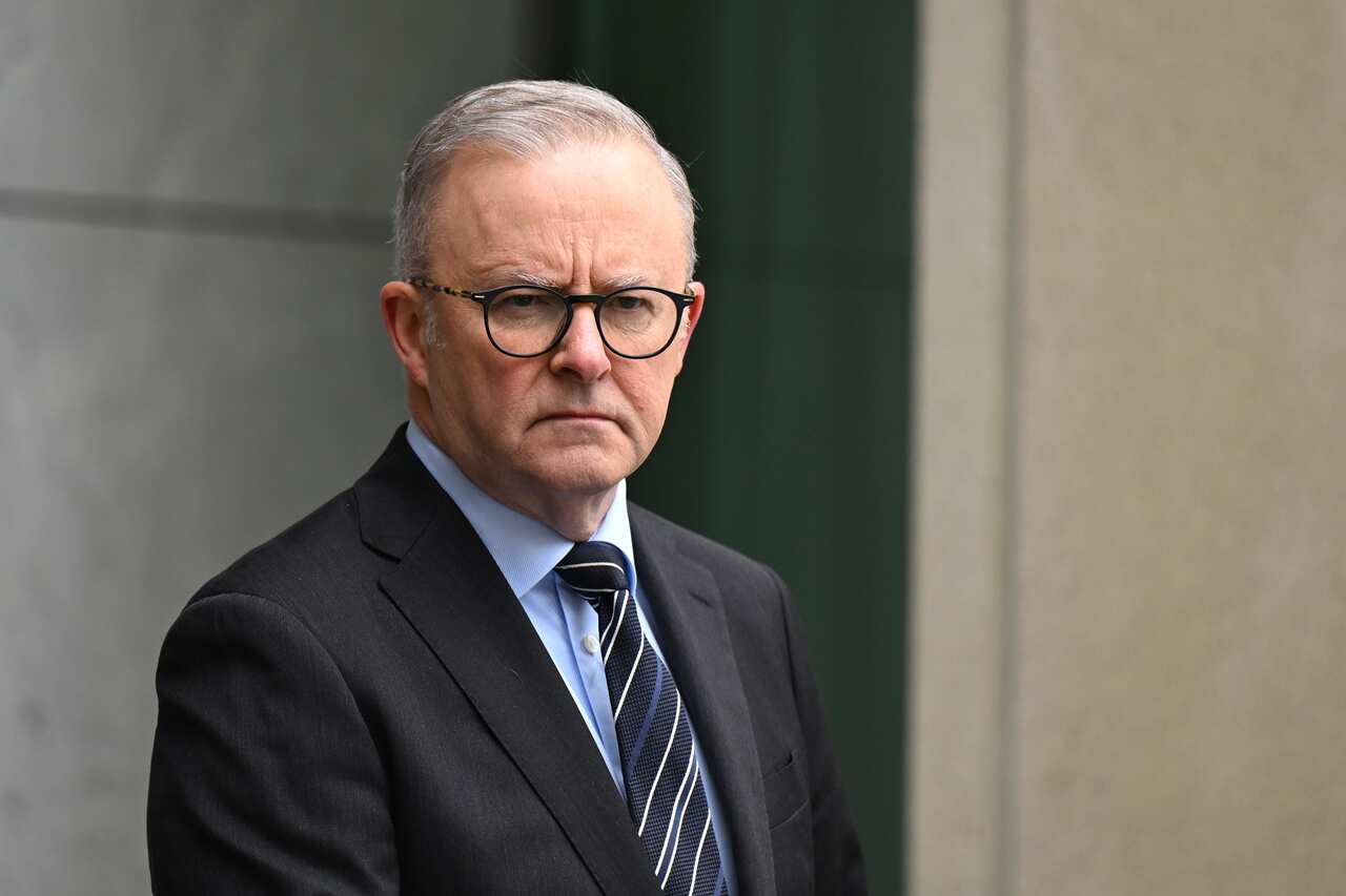 Anthony Albanese, wearing a suit, tie, and glasses, is listening during a press conference.
