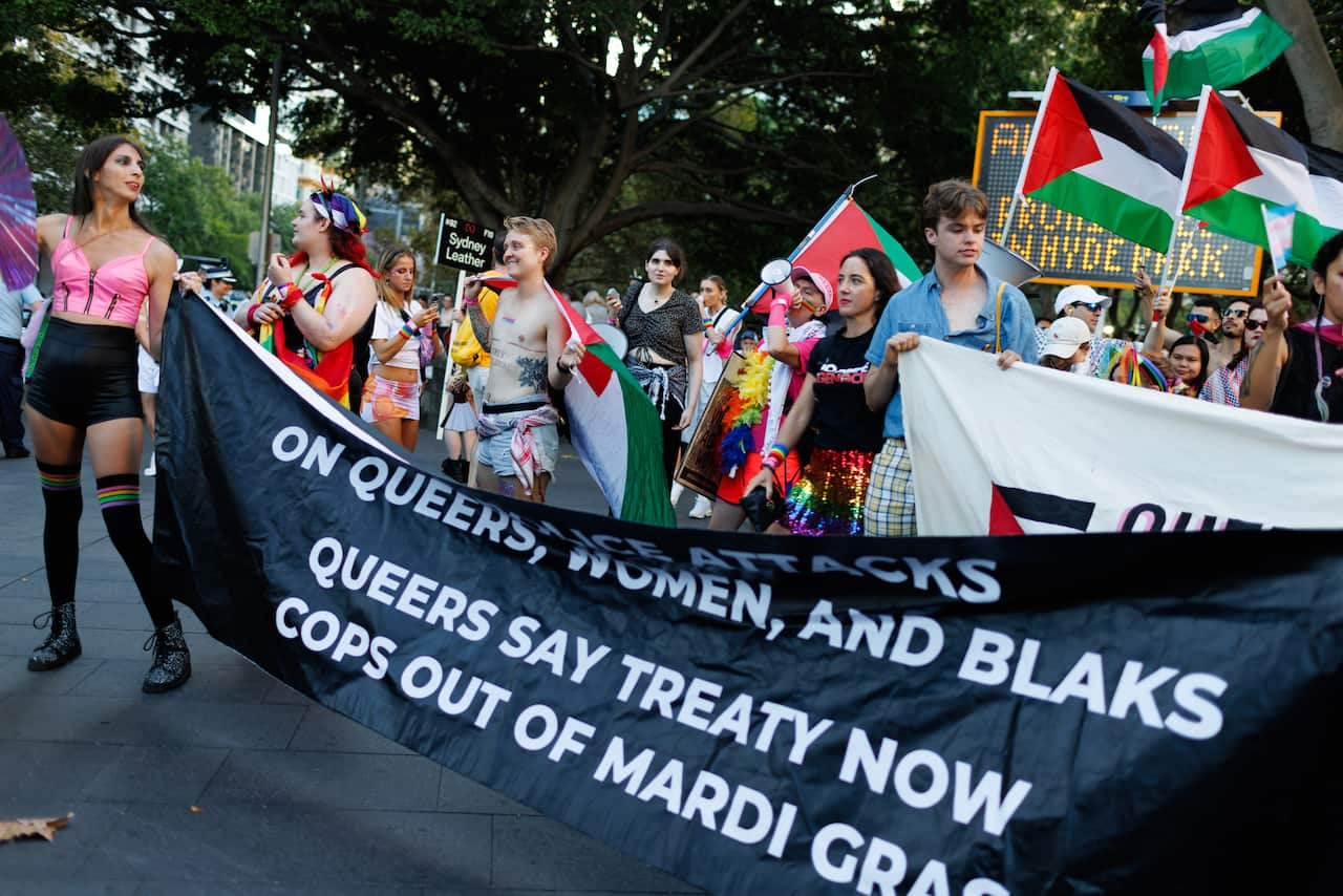 A group of people hold a black banner reading "Queers say treaty now. Cops out of Mardi Gras"