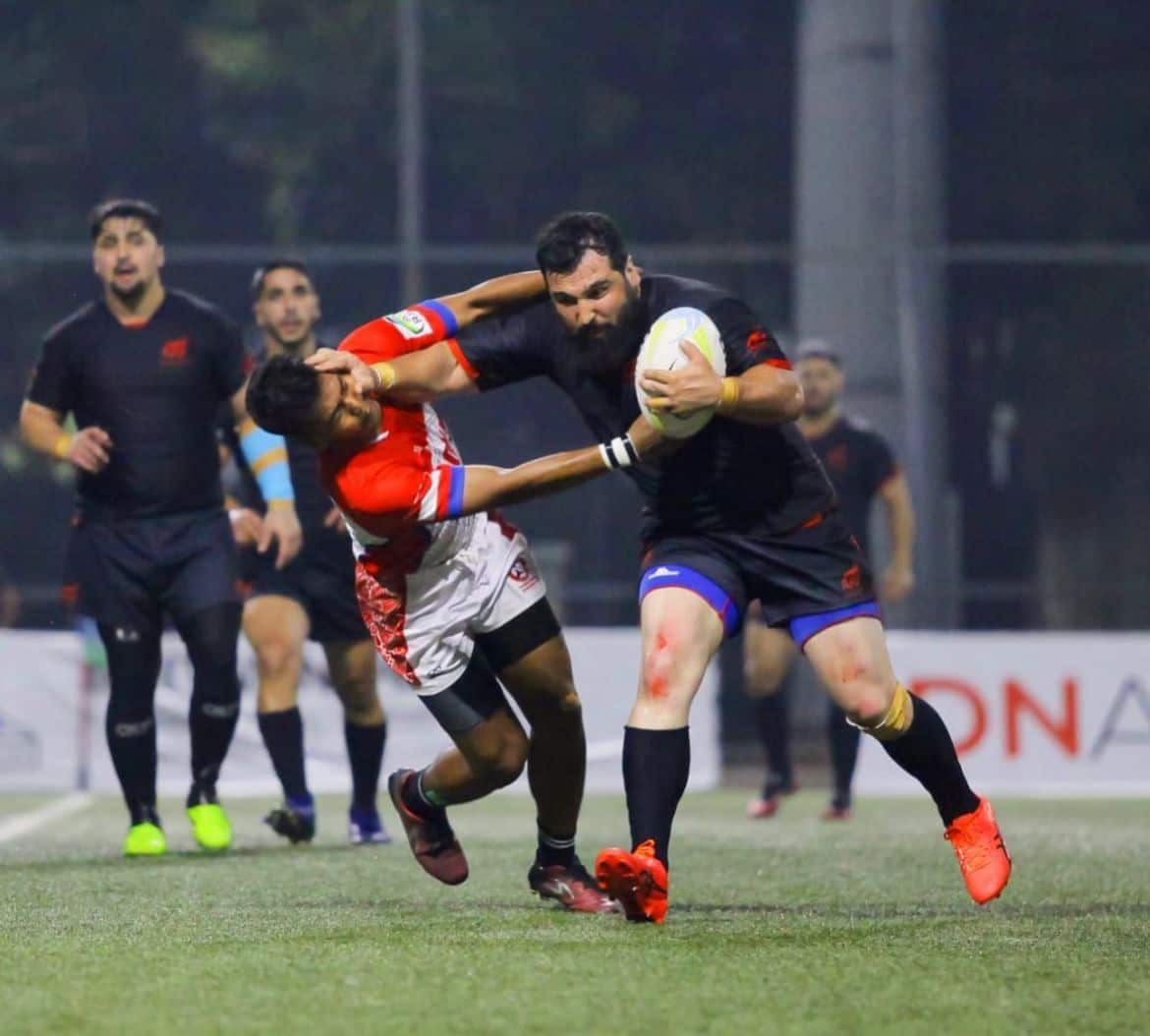 A football player runs with a ball, fending off a defender.