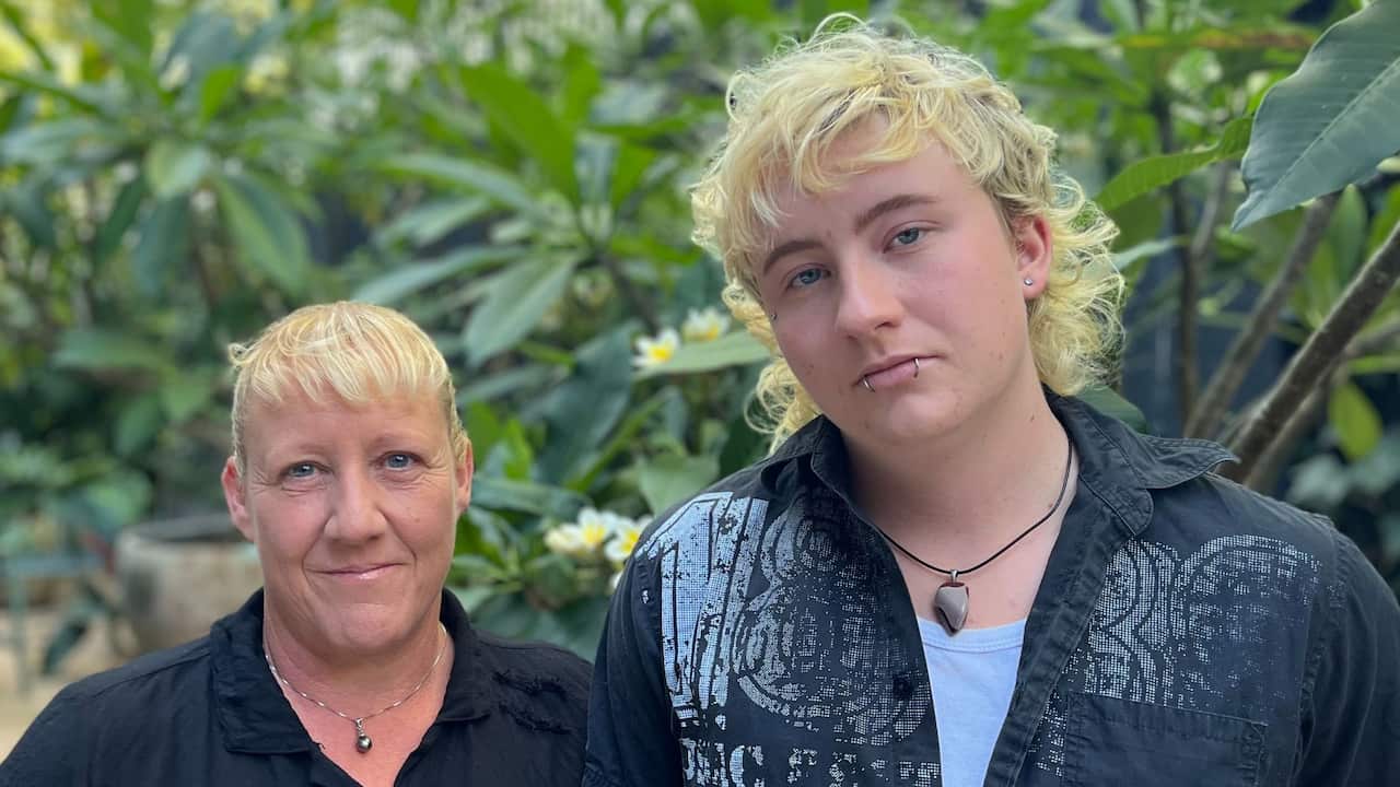 a closeup of a middle aged woman and a young man in a green courtyard - both with blonde hair