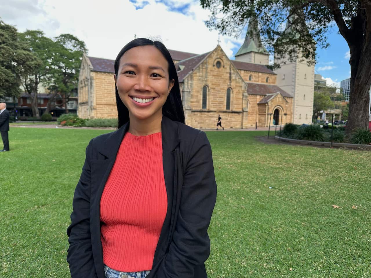 A woman in a red shirt and black jacket smiles to camera