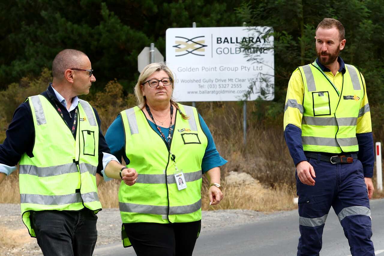 Three people wearing hi-vis vests walk in front of a sign reading "Ballarat Gold Mine" 