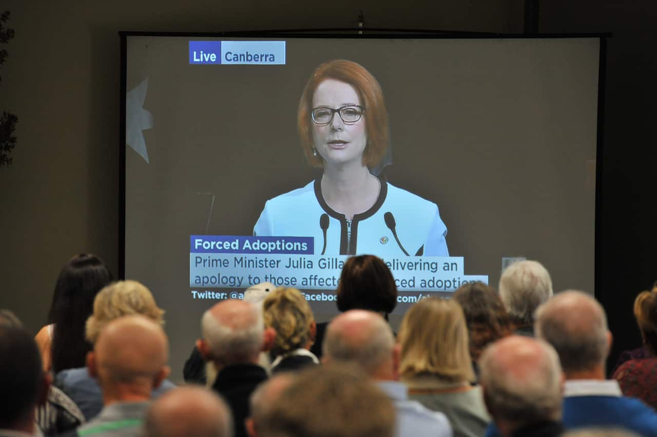 A woman speaks on TV as a group of people look on