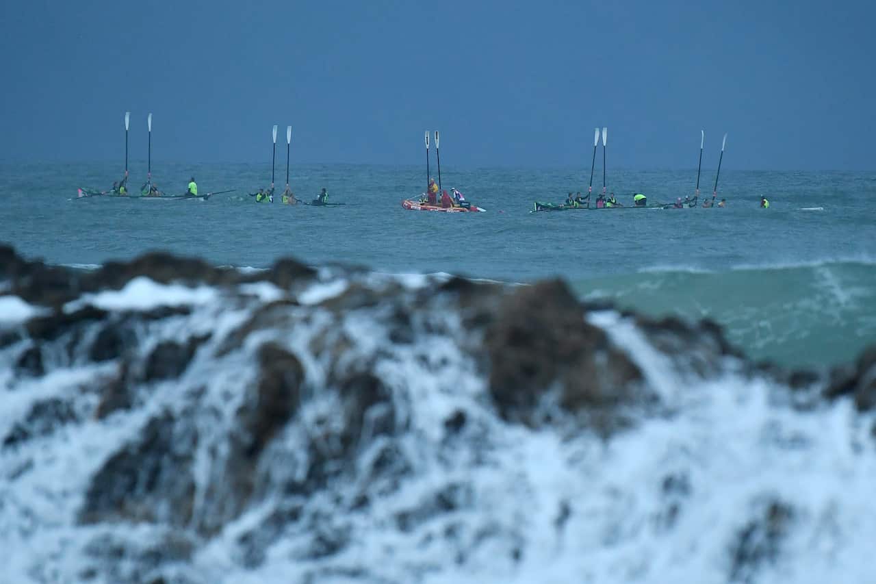 A row of rescue boats in the water, with people in them raising oars.
