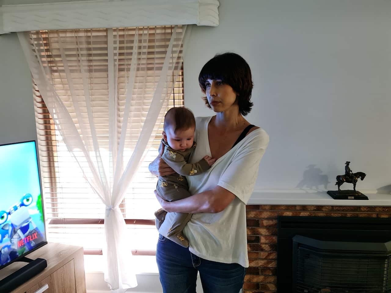 Brooke Haebich, wearing a white T-shirt and jeans, holds her baby in her arms. 