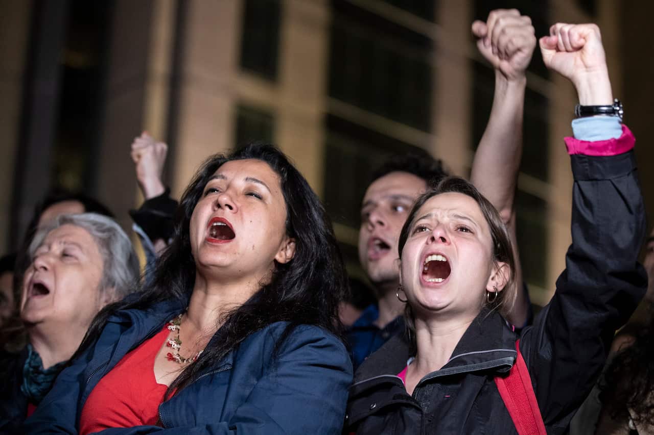 Protestors shout with their arms raised in the air. 