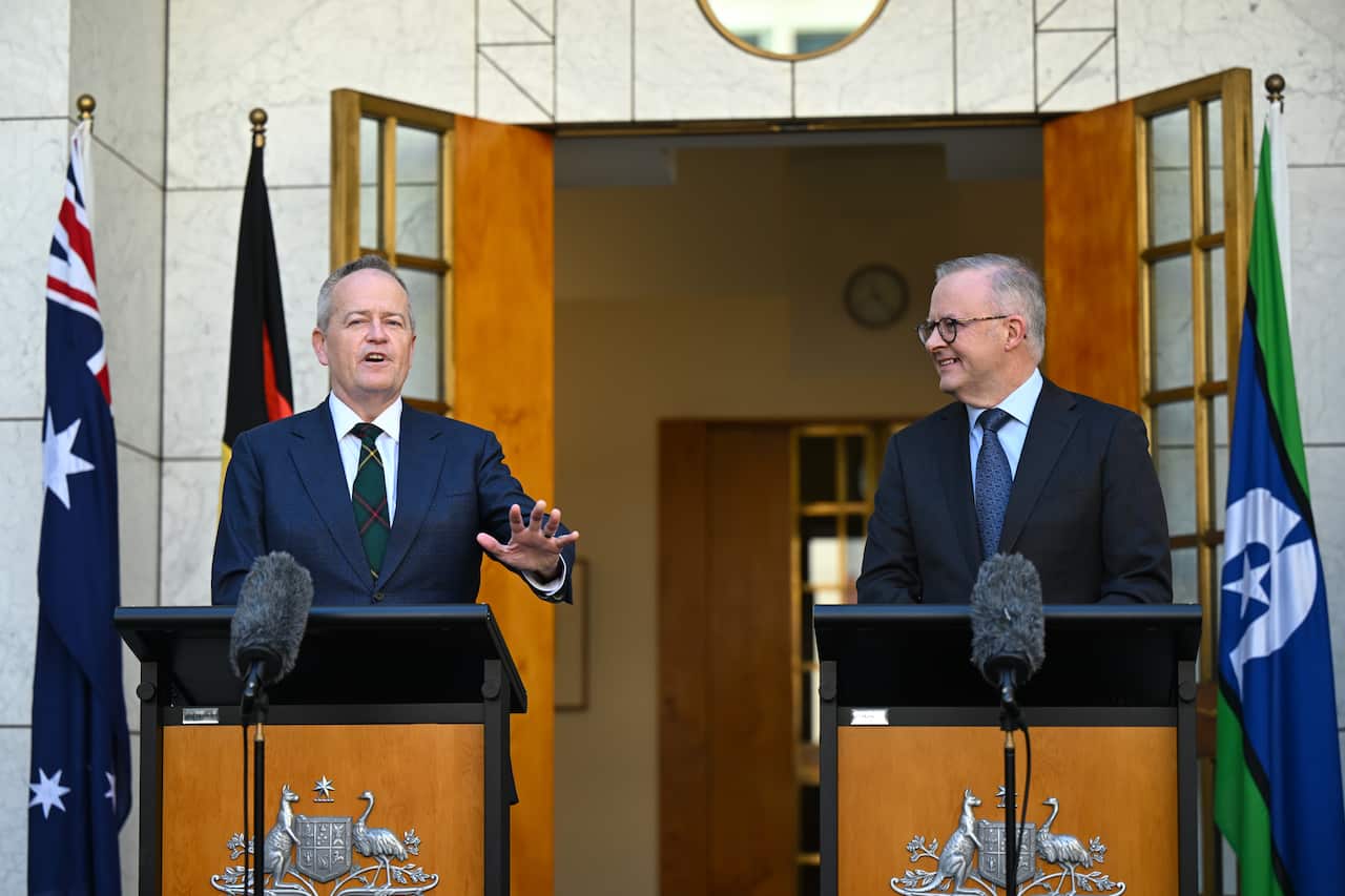 Two men in suits, standing in front of lecterns at Parliament House.