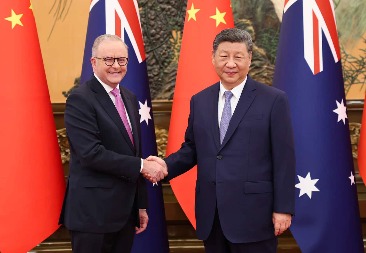 Two men in dark suits shake hands standing in front of the flags of China and Australia 