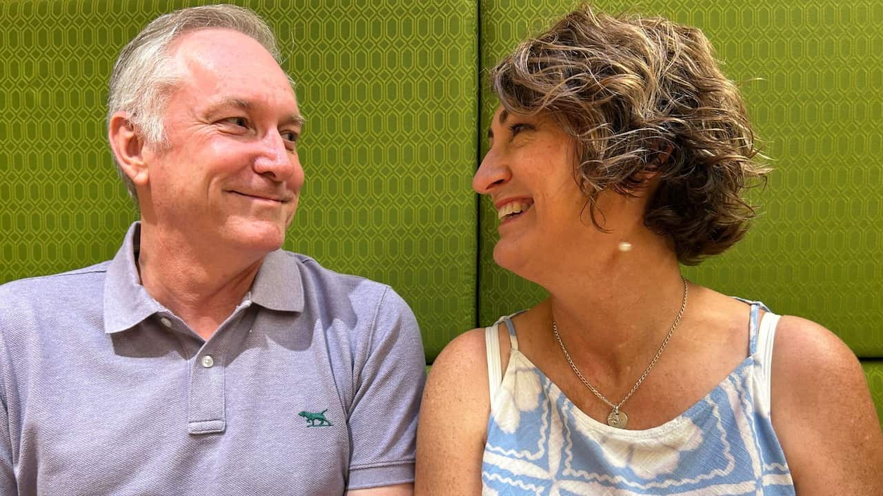 a middle aged man and woman smile warmly at each other, sitting next to each other in a green booth