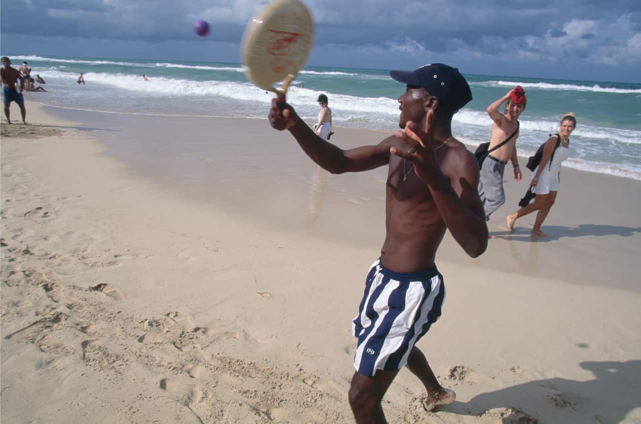 A person with black skin is playing badminton on the beach near the water.