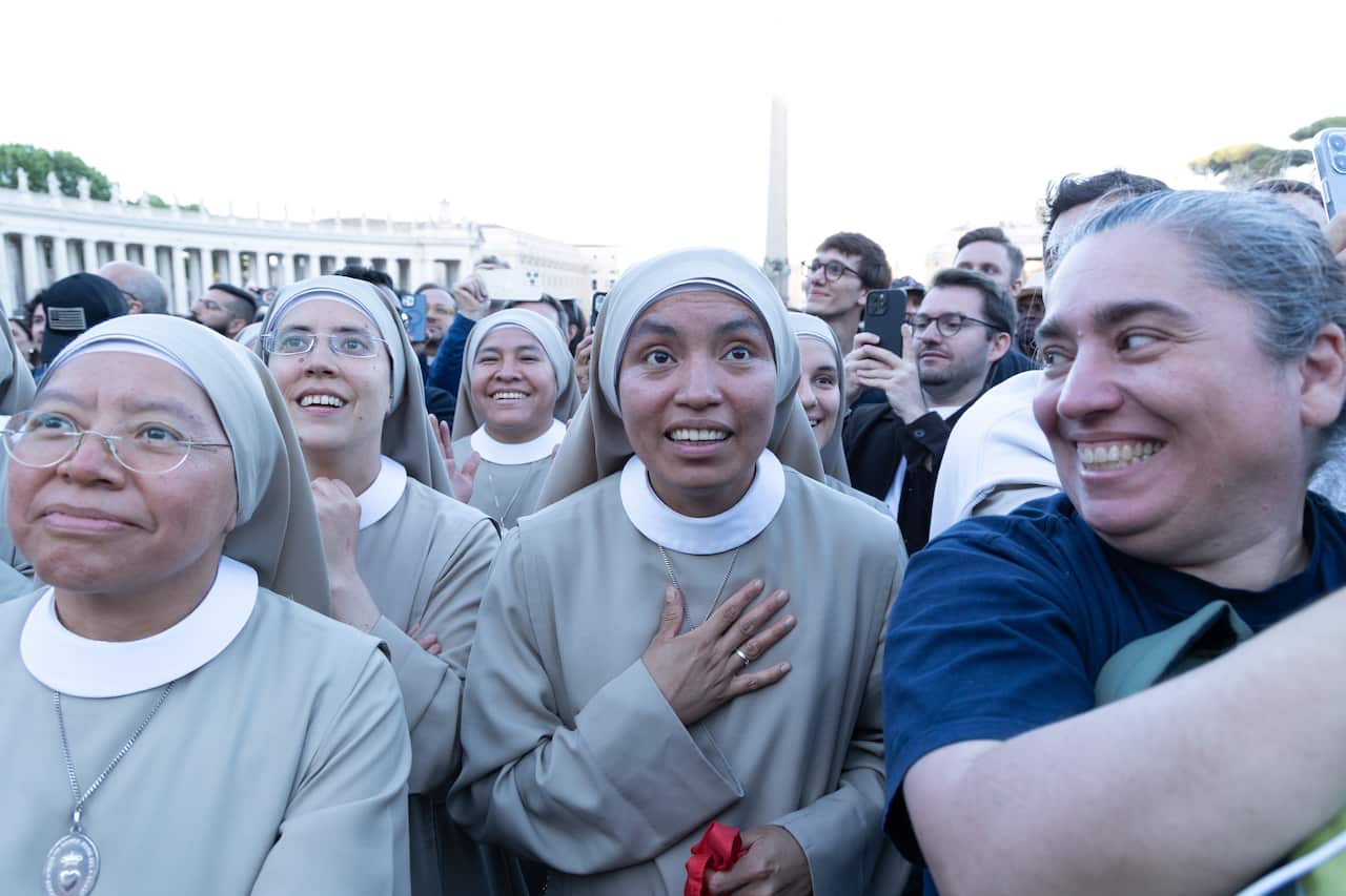 A group of nuns in grey habits look forward with enraptured expressions.