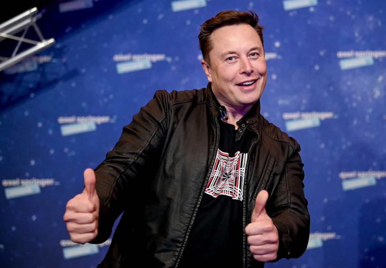 Elon Musk standing and holding two thumbs up