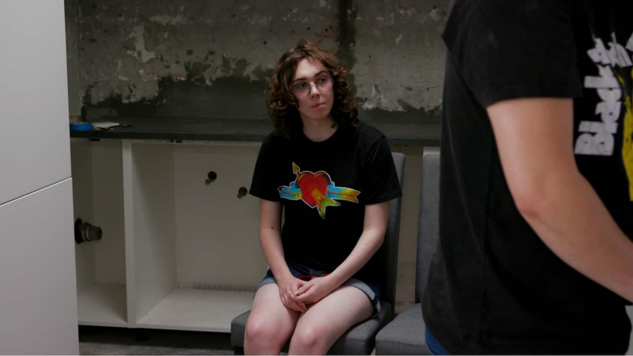 A woman wearing a black t-shirt with a rose pattern in the middle sitting on a chair inside