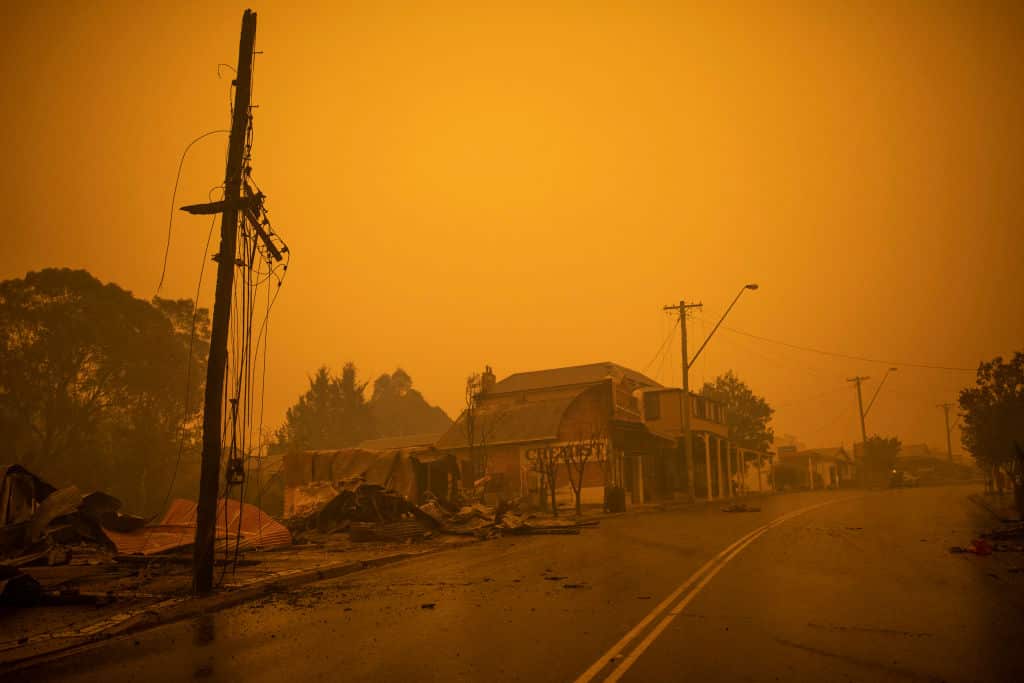 A few houses along a road flanked by trees, surrounded by an orange sky.
