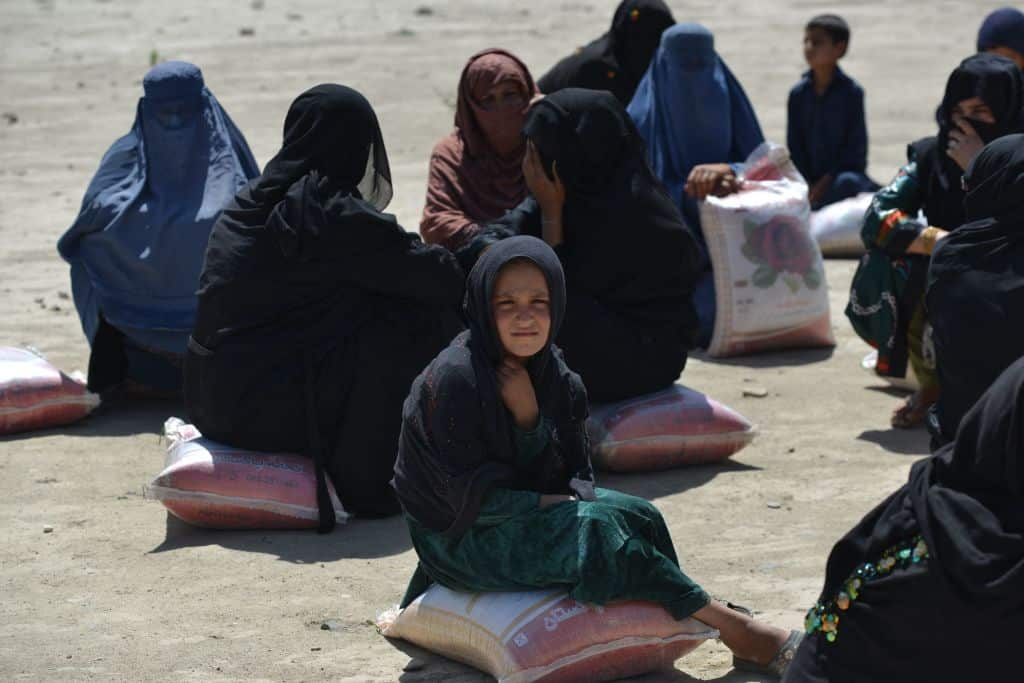 People sit on sacks of rice distributed to people in need by the Afghan Ministry of Refugees in cooperation with China, in Kabul on 8 June 2022.