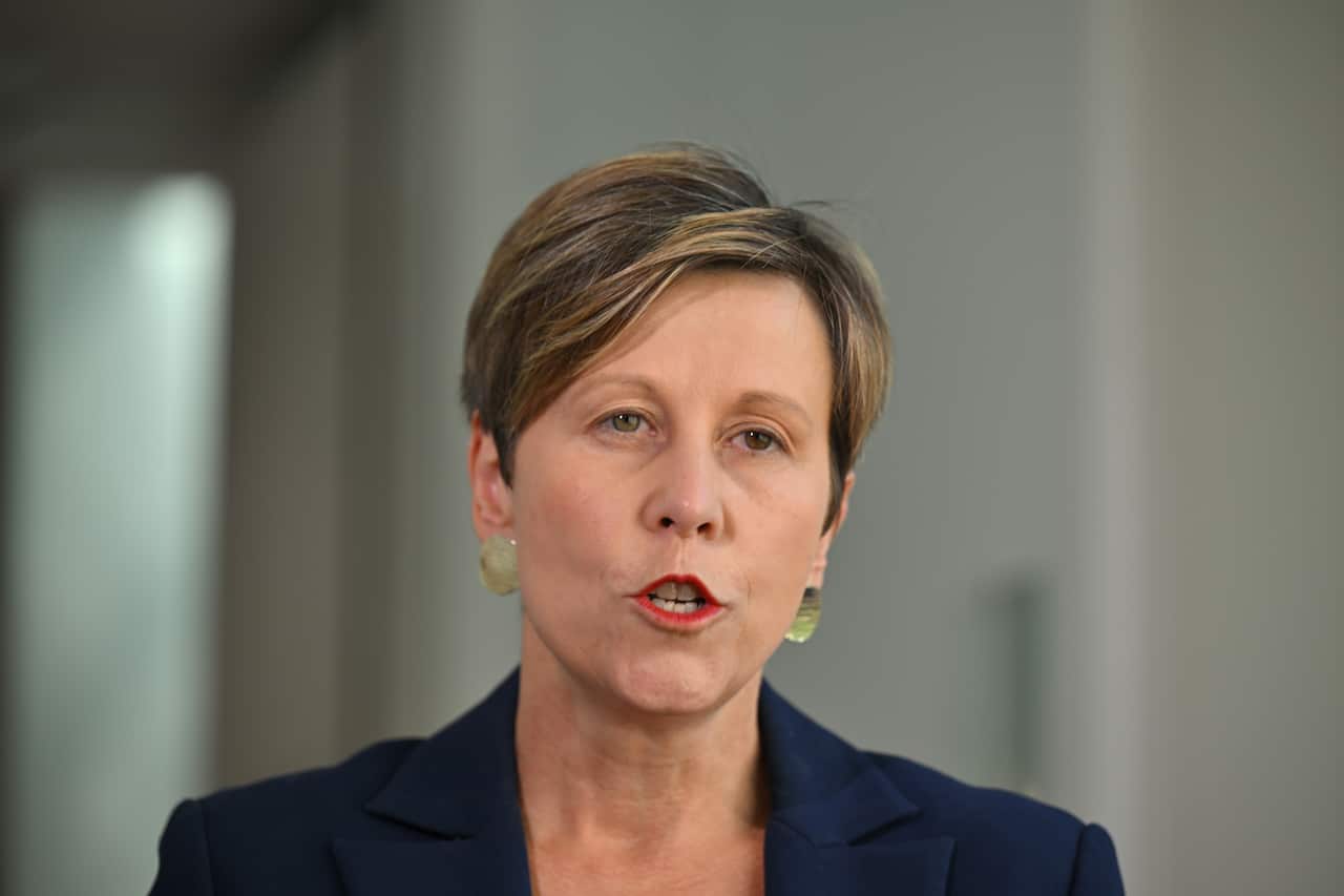 A woman with short hair wearing a suit speaks to the camera.