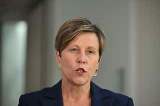A woman with short hair wearing a suit speaks to the camera.