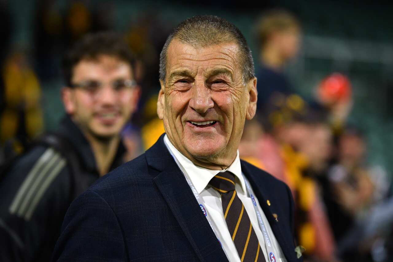 A man in a blue suit, white shirt, and yellow and brown striped tie smiles.