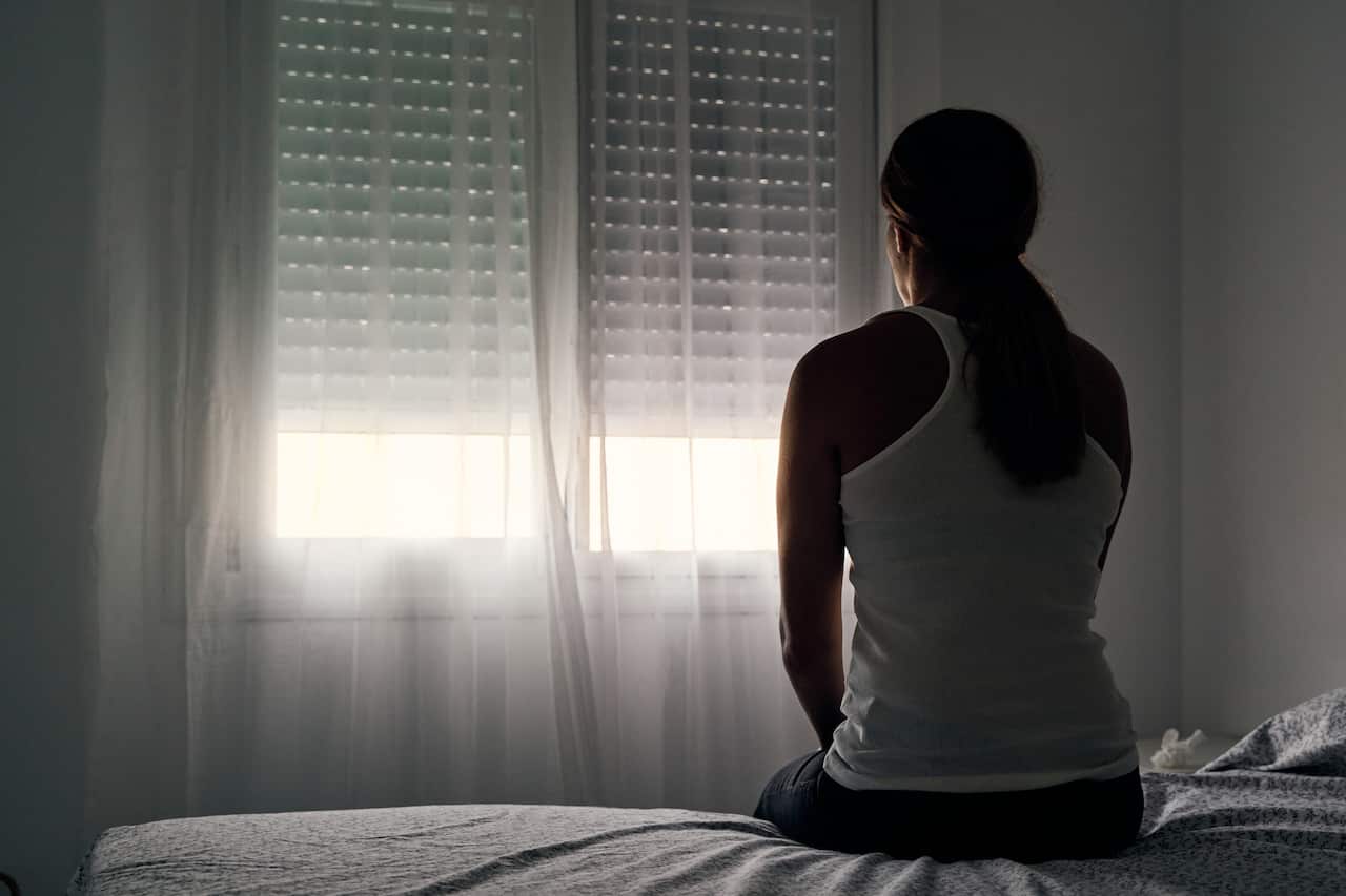 Rear view of an unrecognizable abused woman sitting on her bed looking out the window.