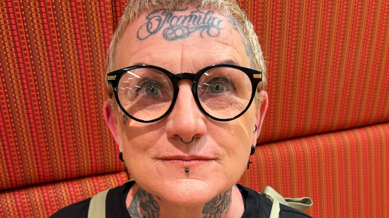 a middle aged woman with short hair, thick framed glasses, septum and lip piercings and a forehead tattoo that says 'Familia'