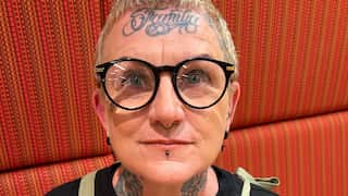 a middle aged woman with short hair, thick framed glasses, septum and lip piercings and a forehead tattoo that says 'Familia'