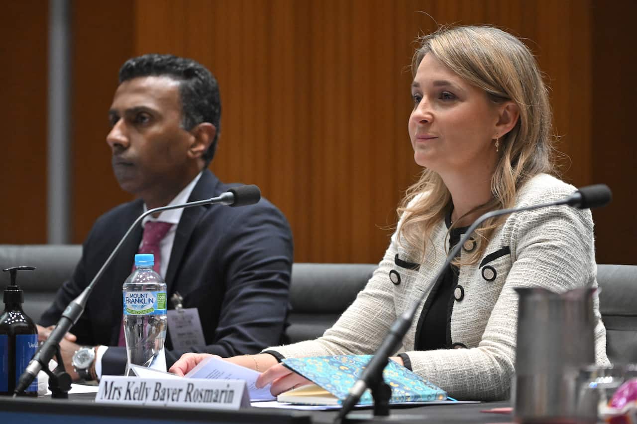 A man and a woman seated at a desk in front of microphones.