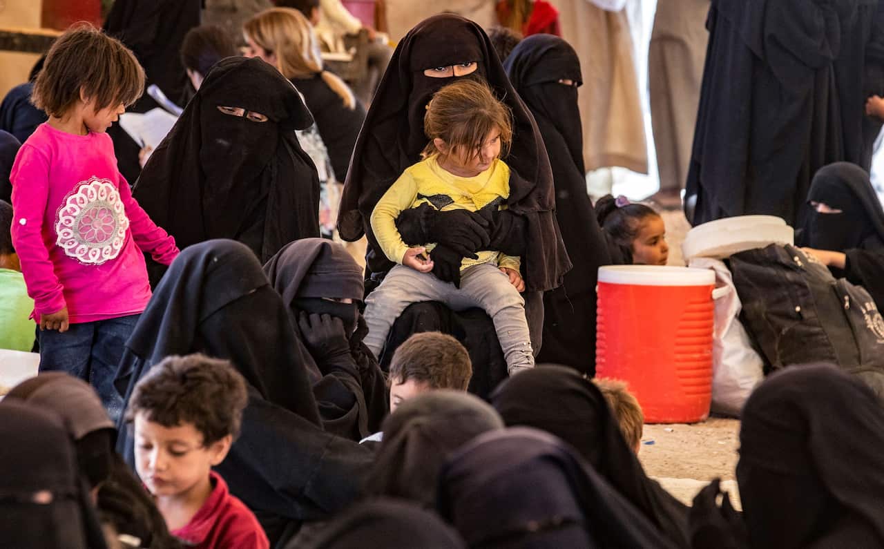 Women in niqabs and children are gathered around.
